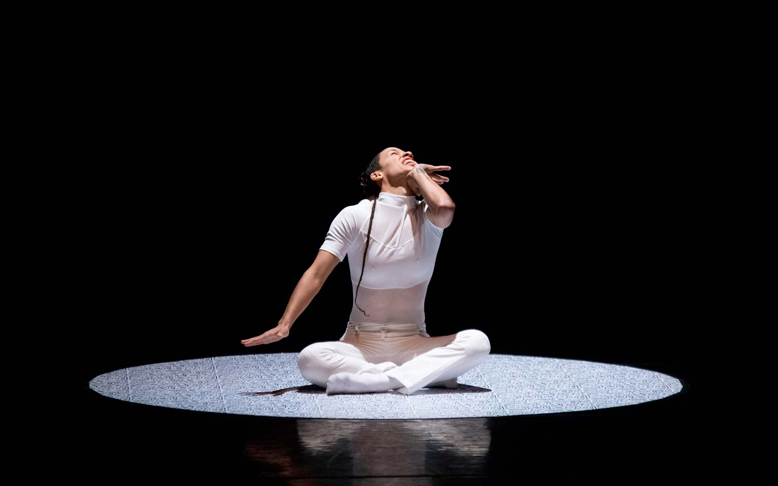 Union PDX - Festival:21 artist Evelyn Tejeda performs her work 'Impossible to Explain'. Photo depicts her seated in the center of a light circle with a contorted face | Photography: Jonathan Hsu