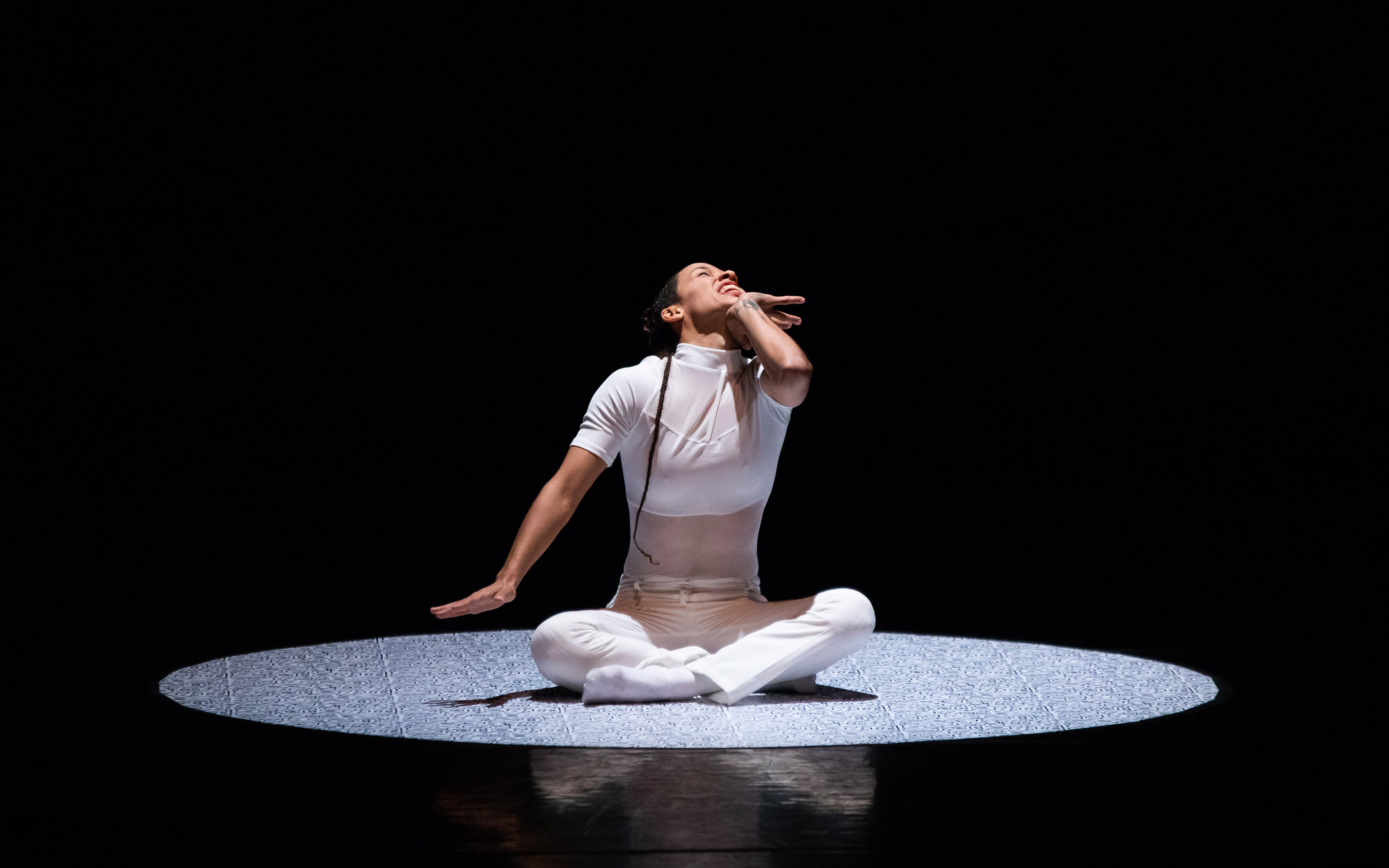Union PDX - Festival:21 artist Evelyn Tejeda performs her work 'Impossible to Explain'. Photo depicts her seated in the center of a light circle with a contorted face | Photography: Jonathan Hsu